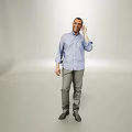 Man Talking on Phone in Blue Shirt and Gray Pants Standing Against Gray Background
