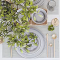 Stylish Tableware Set with Green Plants Wine Glasses Plates and Candle Holders on White Table