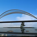Modern White Arch Bridge Spanning Water Under Blue Sky With Clouds Reflection And Island Trees