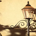 Vintage Outdoor Lamp With Ornate Metal Scroll Design And Glass Shade Casting Shadow On Wall