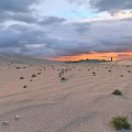 Breathtaking Desert Dune Landscape At Warm Sunset With Camel Caravan Under Dramatic Cloudy Evening Sky