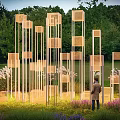 Outdoor Art Installation With Vertical Square Structures Person Grass Purple Flowers Trees Evening Sky