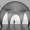 Black Arched Net Like Art Installation In White Gallery With Person Standing Beneath