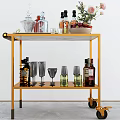 Golden Bar Cart With Glass Top Holding Bottles Glasses And Flower Vase