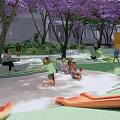 Residential Landscape With Purple Flowering Trees Children Playing On Slide And Adults Resting