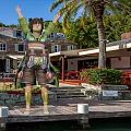 Game Movie Character in Green Outfit with Arms Raised on Wooden Deck by Palm Trees