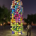 Colorful Illuminated Tower Installation With Trees And Person Standing At Night