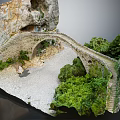 Ancient Stone Bridge In Rocky Cliffs With Green Trees And Gravel Path