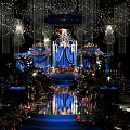Luxurious Banquet Hall With Blue Stage Crystal Chandeliers Floral Decorations Elegant Lighting And Floor Reflections