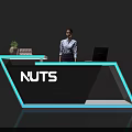 Modern Exhibition Reception Desk With Blue Accents NUTS Logo Laptop Books Plant And Receptionist