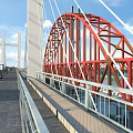 Red Arch Bridge With White Towers Spanning Calm Water Under Blue Sky And Clouds