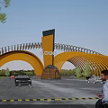 Modern Entrance Gate With Arch Structure Yellow Metal Frame Logo Pillar Cars And Blue Sky