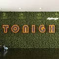 Greenery Wall Design Featuring Orange TONIGH Letters And Lavazza Logo On Wooden Floor With Small Animal Decorations