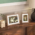 Two Picture Frames with White Flower and Child Art on Wooden Cabinet with Green Plant