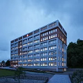 Modern Residential Building Exterior With Illuminated Windows Surrounded By Green Trees At Dusk