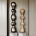 Two Carved Columnar Sculptures With Curved Design In Different Materials Against Light Wood Wall Background