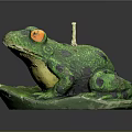 Green Frog Sculpture Sitting On Leaf With Yellow Eyes Black Spots And Candle On Head