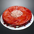 Red Round Cake With Shiny Red Glaze Topped With Crushed Nuts On White Plate
