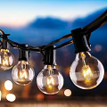 Outdoor String Lights With Transparent Glowing Bulbs Against Twilight Sky And Mountains