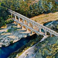 Historic Stone Arch Bridge Spanning River Amidst Green Trees And Natural Landscape