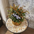 Wooden Brown Vase with Purple Blooms and Green Leaves on Marble Tabletop Near Window
