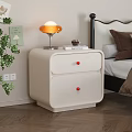Cream Two Drawer Bedside Table With Red Knobs Orange Lamp Book And Green Plant 3d model