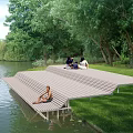 Garden Landscape Design With Sloped Riverside Platform And People Resting Among Trees And Grass