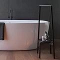 Freestanding White Bathtub By Window With Black Towel Dark Tiled Wall And Toiletries On Shelf