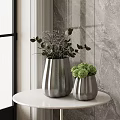 Large And Small Silver Textured Vases With Green Flowers And Purple Foliage On White Table