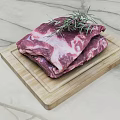 Raw beef slices on wooden cutting board with fresh rosemary