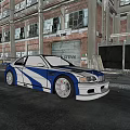Blue and white modified car with large wheels parked in front of old factory building