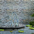 Karesansui Dry Landscape Garden With Stone Wall Backdrop Metal Sculpture Lily Pads And Green Plants