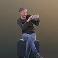 Man Sitting On Black Stool Using Smartphone In Dark Long Sleeve Top And Blue Jeans