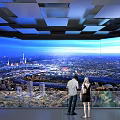 People Enjoying City Panorama At Modern Observation Deck With Glass Railings And Geometric Ceiling Design