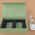 Open Green Box With Black Compartments And White Teacups Teapot On Striped Tabletop