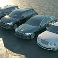 Different Luxury Cars Parked By Waterfront On Stone Pavement Under Sunlight