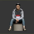 A Man Sitting On Cylindrical Stool Wearing Black Cap Gray Jacket And Blue Jeans