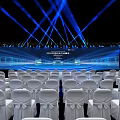 Modern Conference Hall Setup With White Chairs Stage Screen And Blue Lighting
