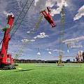 Red And Yellow Cranes At Construction Site With Green Grass And Distant Buildings