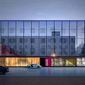 Modern Glass Building Exterior With Sloped Design Trees Street Lamps Vehicles And Brick Pavement