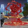 Giant Red Rose Sculpture Illuminated At Night With City Skyline And People Around