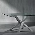 Modern Glass Top Dining Table With Crossed Metal Legs Against Gray Wall And Floor