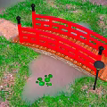 Red Wooden Bridge Over Small Pond With Lily Pads And Green Grass Path