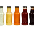 Colorful Condiment Bottles With Black Caps For Sauces On Gray Background