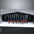 Vanity Fair Stage Setup With Group Of Performers In Orange Outfits On White Platform