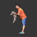 A man holding a cat in orange T-shirt and blue shorts against black background