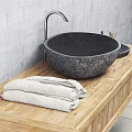 Black Stone Sink with Silver Faucet on Wooden Countertop and Stone Containers Against Gray Wall