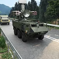 Multiple Green Military Functional Vehicles with Weapon Systems Driving on Road in Mountain and Trees