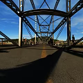 Steel Bridge Structure With Blue Sky People Walking And Road Surface Shadows