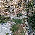 Aerial View Of Steep Rocky Terrain With Lush Green Vegetation And Path Near Water